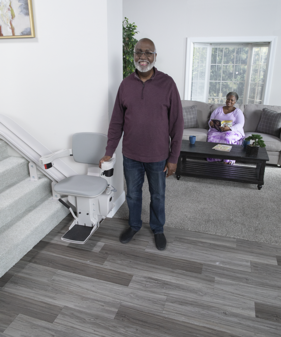 The Bruno Elite curved stairlift with a man standing beside it. His wife is relaxing in the living room behind him.