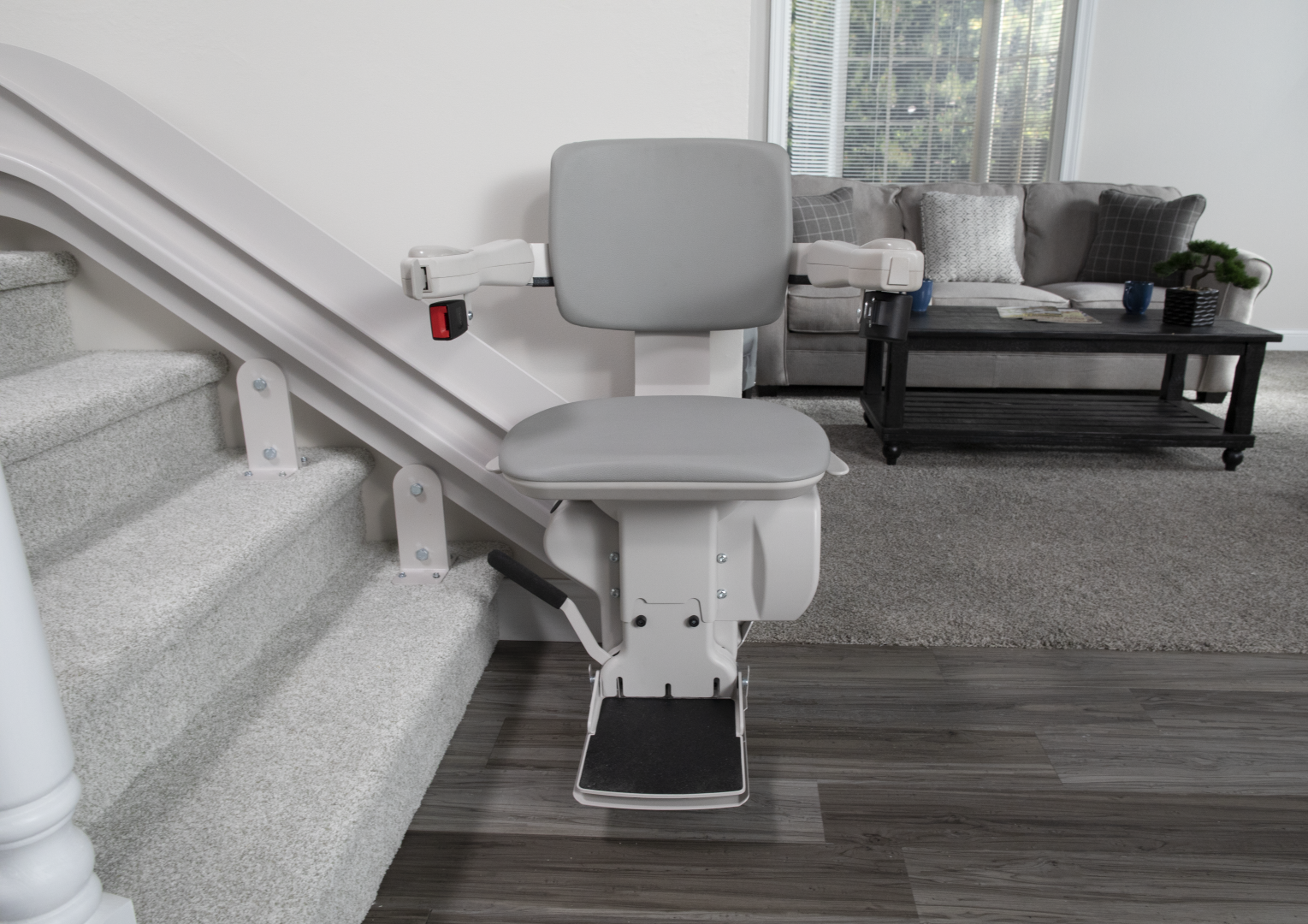 Elite indoor curved stairlift chair beauty shot The chair of the Elite indoor curved stairlift at the bottom of a staircase, with a tidy living room in the background