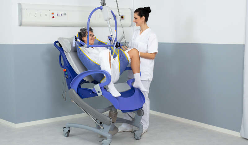 Patient with nurse using Maxi Sky 2 A woman is being lifted with assistance from a nurse using a Maxi Sky 2 ceiling lift.