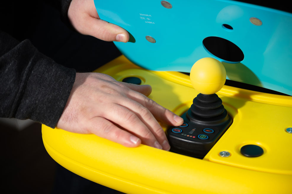 A close up of the Explorer Mini tray, with the top cover lifted up to show the full joystick below. The cover is turquoise and the joystick knob is bright yellow.