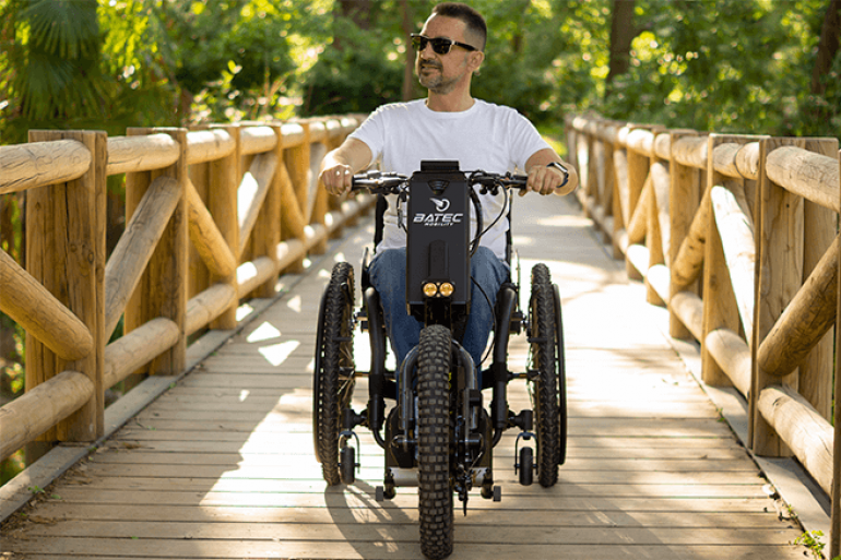 A man using a Batec Scrambler handbike rides across a wooden bridge
