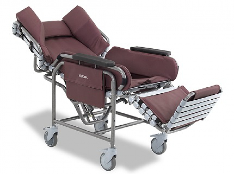 The Broda Centric positioning wheelchair with burgundy padding, shown in a reclined position with the footrest extended.