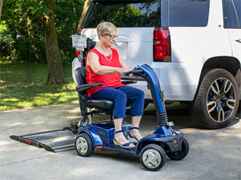 A woman drives her mobility scooter off of the Out-Sider scooter lift that is installed on the back of her vehicle.