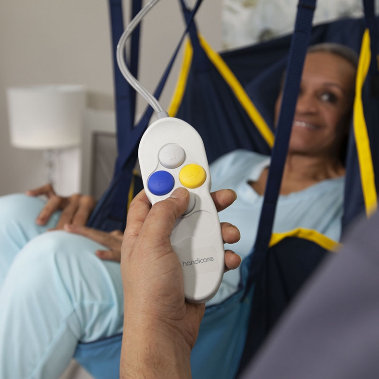 A closeup of the hand control for the lift, showing the 4 control buttons. A patient in a sling is smiling in the background.