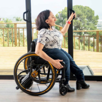 A woman using a manual wheelchair with SmartDrive slides open the glass door leading onto a large wooden patio overlooking a green cityscape. thumbnail