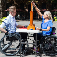 Two people using SmartDrives playing a board game at an outdoor table in the sunshine.