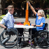 Two people using SmartDrives playing a board game. thumbnail Two people using SmartDrives playing a board game at an outdoor table in the sunshine. thumbnail