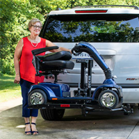 An Out-Sider scooter lift is lifted on the back of an SUV with a woman standing beside it, smiling. thumbnail