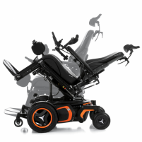 The F5 Corpus VS standing wheelchair is shown in a tilted position. It has orange accents and black rehab seating, including a headrest.