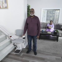 The Bruno Elite curved stairlift with a man standing beside it. His wife is relaxing in the living room behind him. thumbnail