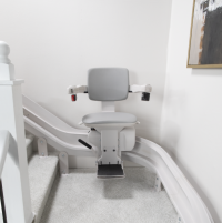 The Bruno Elite Curved stairlift installed on a white staircase, with the chair midway between the top and bottom of the stairs. thumbnail