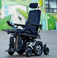 The Corpus M5 power chair with white accents, rehab seating and multiple user controls. It sits in front of a warehouse painted with urban artwork. thumbnail