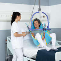 A smiling woman is being lifted from her hospital bed with a caregiver's assistance, using the Maxi Sky 2 ceiling lift thumbnail