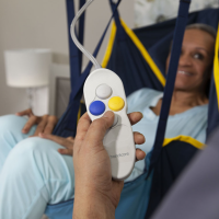 A closeup of the hand control for the lift, showing the 4 control buttons. A patient in a sling is smiling in the background. thumbnail