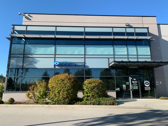 The mirrored exterior of the Burnaby showroom with logoed vans parked in front.