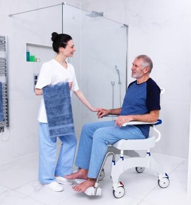 A man sits on a shower commode in his bathroom.